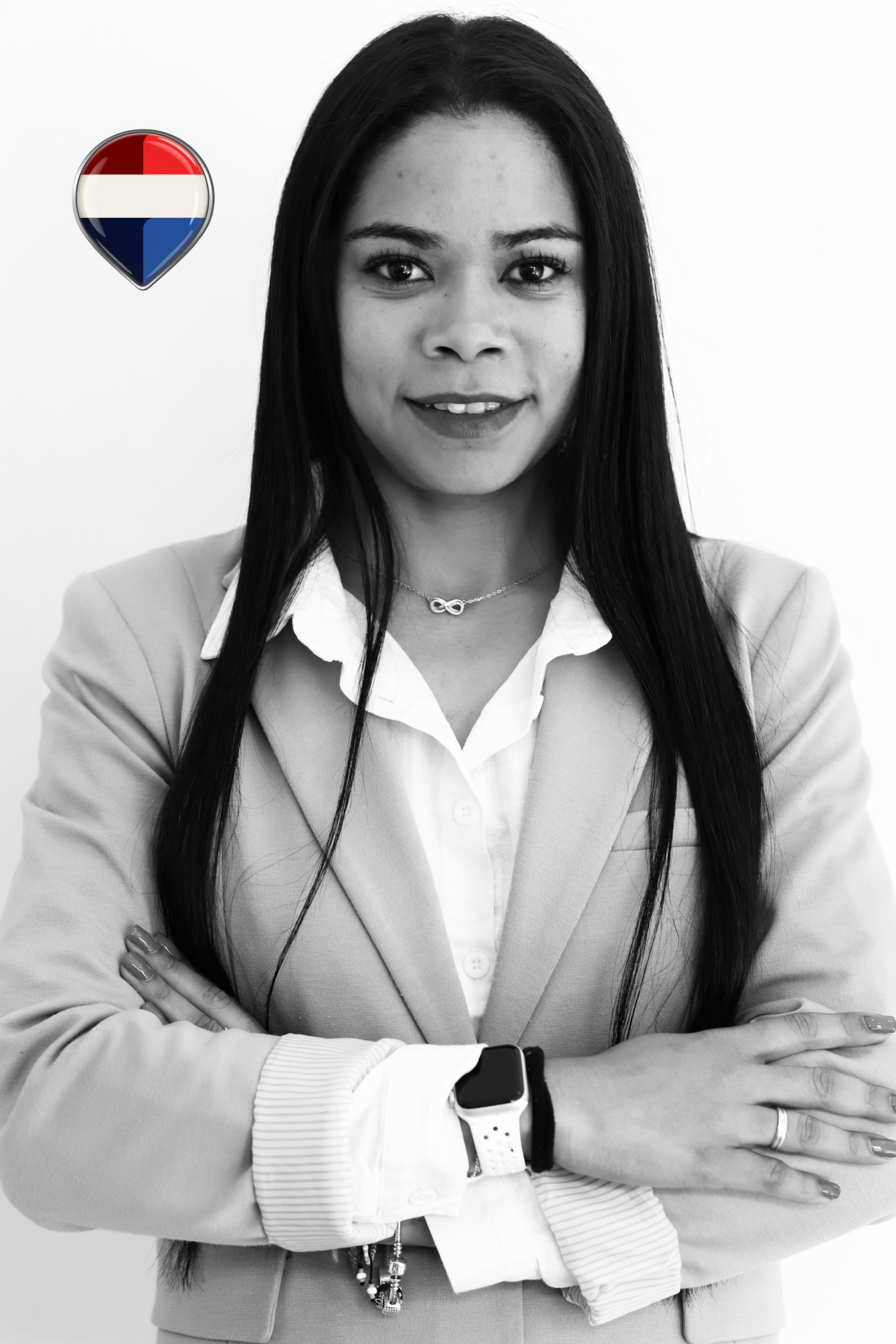 Mujer de negocios con traje claro y blusa blanca, sonriendo mientras cruza los brazos. Presenta un reloj en la muñeca y un collar con símbolo de infinito. Fondo blanco y logotipo con los colores de la bandera de los Países Bajos en la esquina superior izquierda.